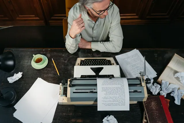 An overhead shot of an adult man writing with a typewriter in a vintage-themed study. Weak thesis, list structure, repetition, and unsupported claim problems