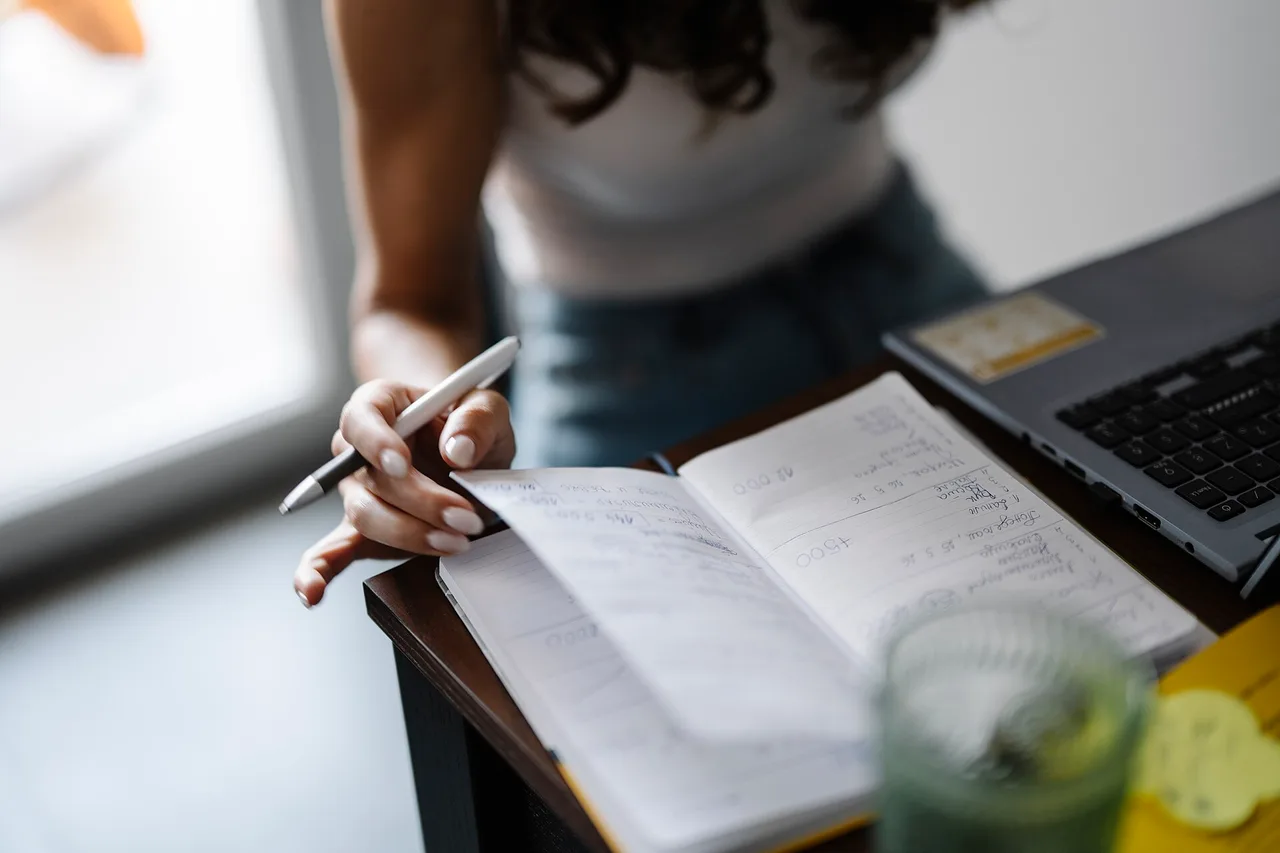 Person turning pages in a notebook beside a laptop