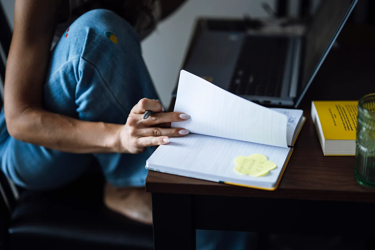 Person writing notes in an open notebook at a table